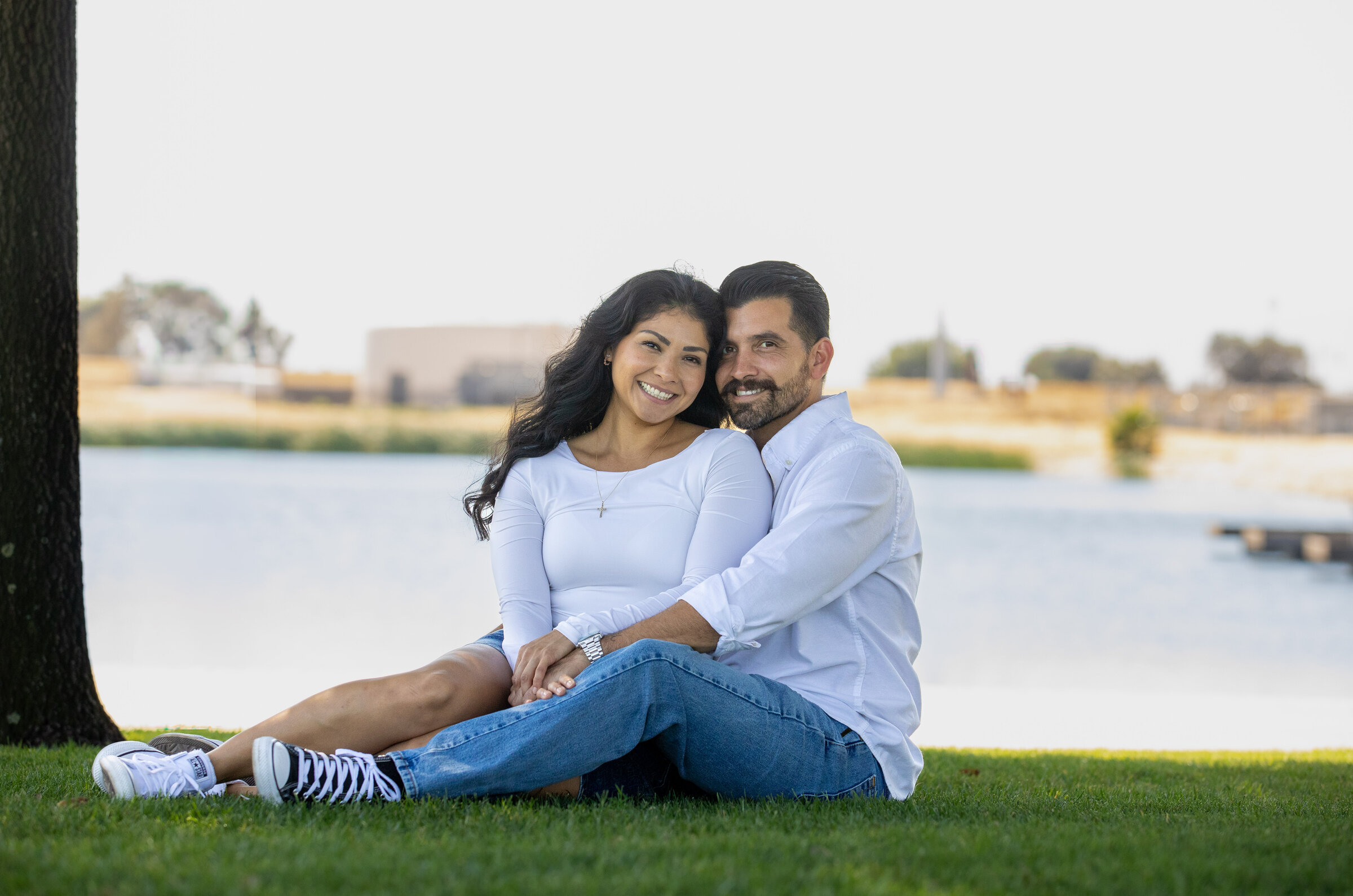 Engaged couple sitting on the grass by a lake in the Reno-Tahoe area
